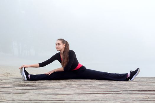 Young pretty slim fitness sporty woman does stretching exercises during training workout outdoor