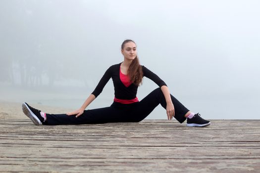 Young pretty slim fitness sporty woman does stretching exercises during training workout outdoor