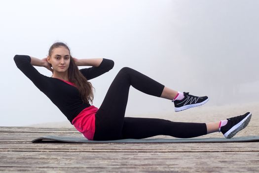 Young pretty slim fitness sporty woman does abs exercises during training workout outdoor
