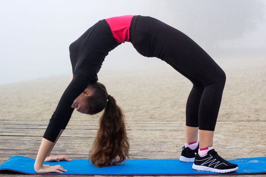 Young pretty slim fitness sporty woman does stretching exercises during training workout outdoor