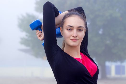 Young pretty slim fitness sporty woman exercises with weights dumbells during training workout outdoor