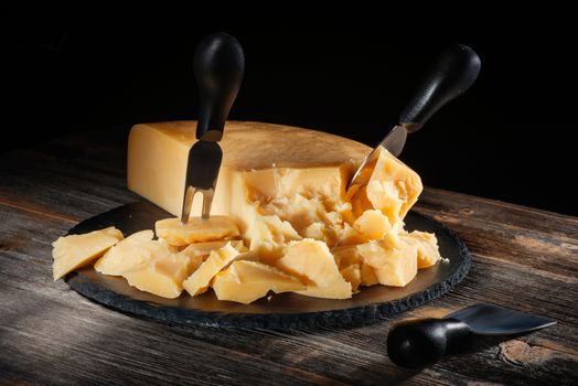 Cheese parmesan with a set of knives on a black round slate board in style a rustic