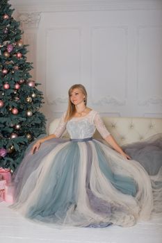 Blonde girl in evening dress sitting on a sofa in the new year eve