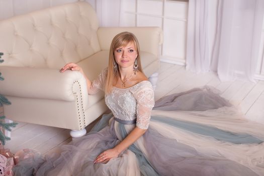 Attractive young girl sitting on the floor, dressed in a white gown with a train dinnym