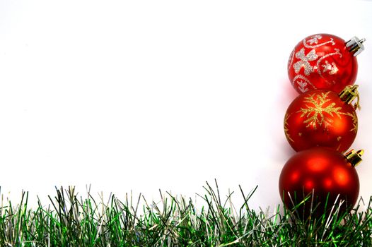 Three christmas balls and a green garland placing vertically right on a white background