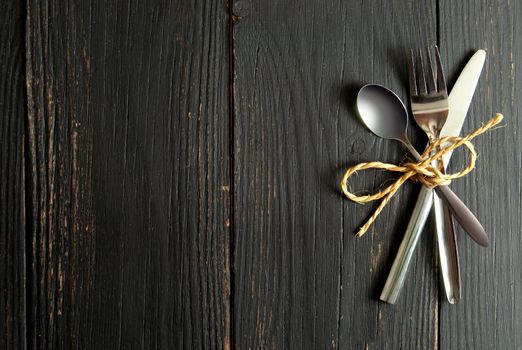 Fork, knife and spoon  tied together on a wooden table with space