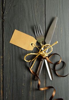 Fork and knife tied together on a wooden table background with tag