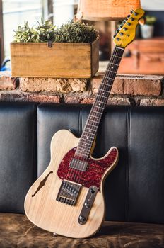 Electric Guitar Leaning Against a Couch. Electric Guitar with Natural Wood Finish Still Life.