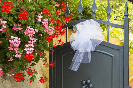 View of a bridal bow put on an iron gate with colorful flowers on the left