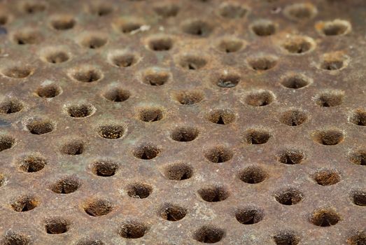 Rusty metal surface with round holes arranged in a row. Grunge background. Selective focus close-up image