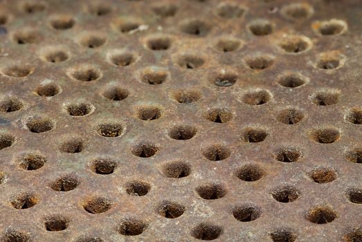 Rusty metal surface with round holes arranged in a row. Grunge background. Selective focus close-up image