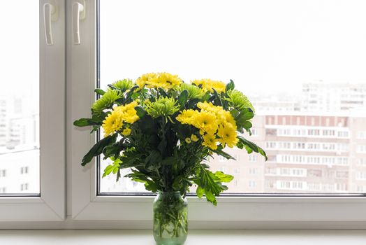 Bouquet of yellow chrysanthemums and green stands on the windowsill