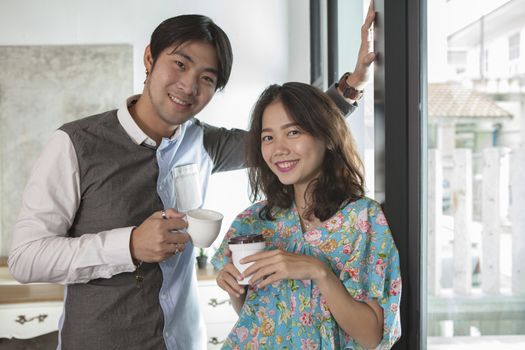 couples of asian young man and woman with coffee cup in hand standing relaxing in home living room