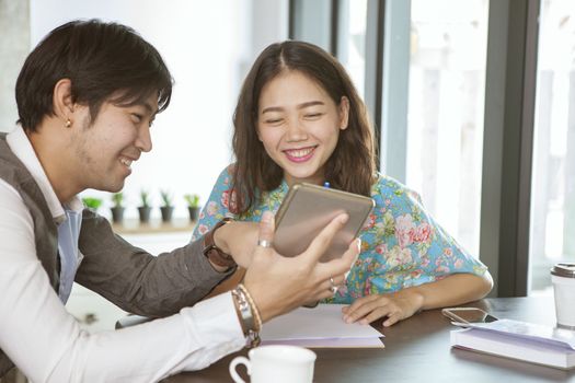 asian younger man and woman relaxing with computer tablet in hand in coffee shop ,social media and digital connecting technology lifestyle