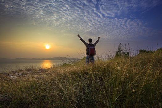 trekker man rising victory hand at nature trail with sun set sky