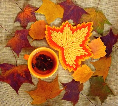 Mock-up autumn. Orange cup with tea on a background of autumn leaves. Crafts leaf, crochet, felt. Background - coarse texture