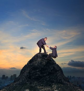 two of asian business man helping hand to climbing up to peak of rock mountain abstract of team work and partner for successful business 