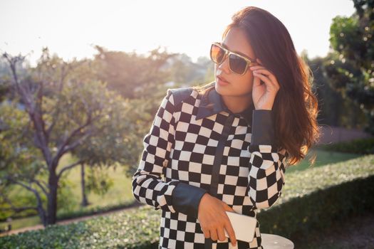 portrait of beautiful chick fashion woman wearing sun glasses and smartphone in hand against afternoon light with blur background and copy space