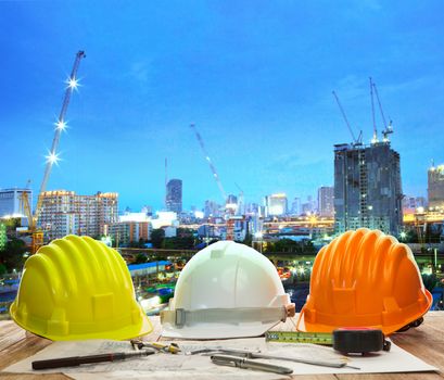 engineer working table with hard hat plan and writing tool against beautiful lighting and urban building construction site use for land and city development backgound