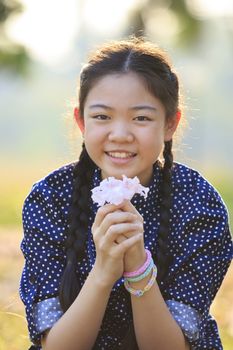 thai 12s years girl sitting on garden field with pink flowers in hand toothy smiling face happiness emotion