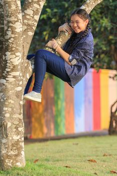 asian girl playing funny face by climbing on tree branch in public park with happiness emotion 