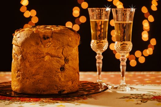 Italian panettone and sparkling wine over a table with Christmas lights on background