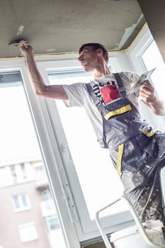 Thirty years old manual worker with wall plastering tools renovating house. Plasterer renovating indoor walls and ceilings with float and plaster.