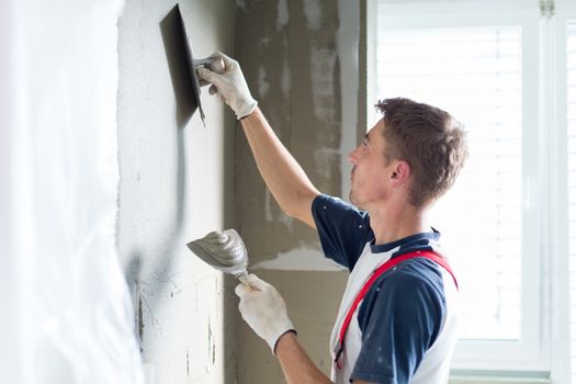 Thirty years old manual worker with wall plastering tools renovating house. Plasterer renovating indoor walls and ceilings with float and plaster.