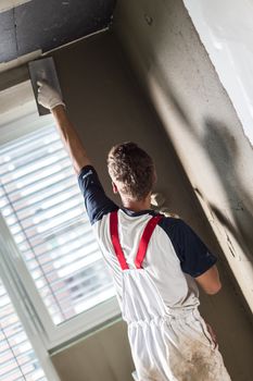 Thirty years old manual worker with wall plastering tools renovating house. Plasterer renovating indoor walls and ceilings with float and plaster.