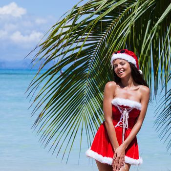 Beautiful woman in Mrs. Claus custume on tropical beach with palms, Christmas vacations concept