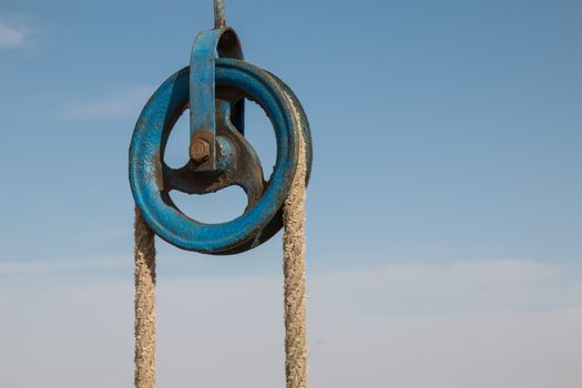 Blue old roller with a rope, part of the well in the desert in Morocco. Important source of the drinking water. Cloudy sky in the background.