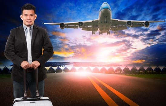 younger asian man and traveling luggage standing against passenger plane flying over airport runway