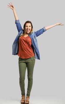 Beautiful happy woman with arms up over a gray background