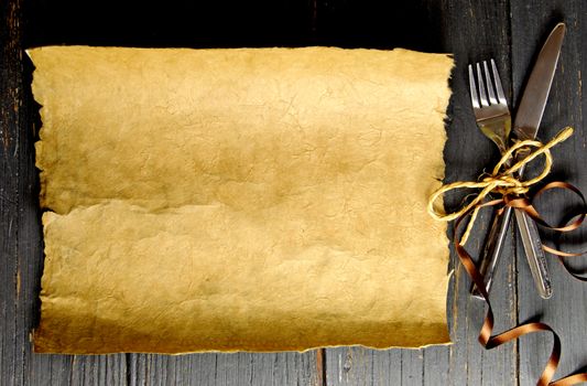 Fork and knife tied with satin ribbon with a blank piece of scroll paper