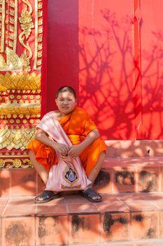 LUMPHUN THAILAND - JAN 8 : thai little monk sitting in front of buddha church door in Pra That Hariphunchai Temple in Lumphun province important buddhist worship place on january 8 , 2016 in lumphun thailand