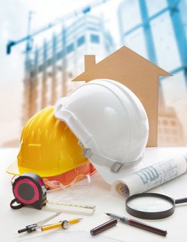 safety helmet blue print plan and construction equipment on architect ,engineer working table with building construction crane background use for construction industry business and civil engineering 
