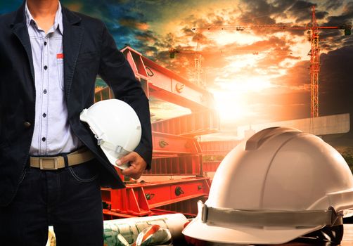 engineer man with white safety helmet standing against working table and building construction scene 