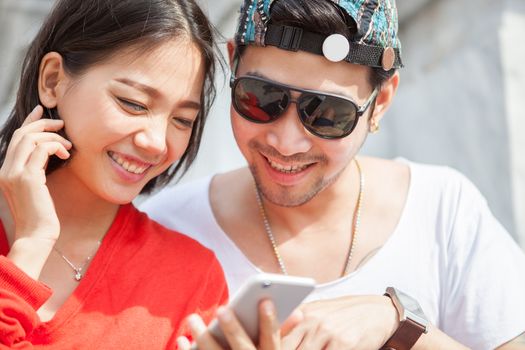 couples of asian younger traveling man and woman reading message in smart phone with happiness face toothy smile