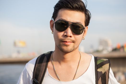 portrait close up head shot of handsome asian man standing with back packer outdoor