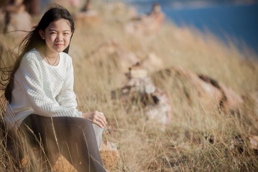 portrait of asian girl relaxing emotion sitting in grass field and windy evening use for teen age leisure and activities traveling vacation time