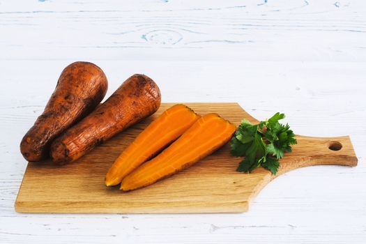 Boiled carrots and parsley on board, light wooden background