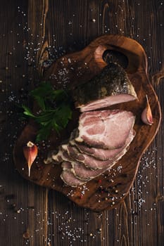 Sliced cold baked pork with herbs on a slate cutting board on wooden background