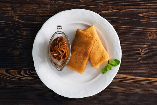 Pancakes with condensed milk on a plate, wooden background