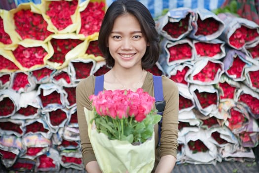 smiling face of younger asian woman with pink roses flower bouquet in hand 