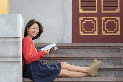 beautiful younger asian traveling woman relaxing and reading traveler guide book in thailand destination