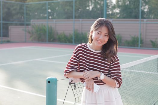 portrait of beautiful young asian woman wearing white clothes skirt in tennis course with happy face 