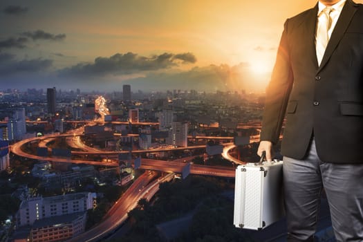 business man and metal briefcase luggage in hand standing against express way of capital town and sun rising sky