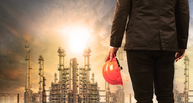 engineering man with safety helmet standing in industry estate against sun rising above oil refinery plant 