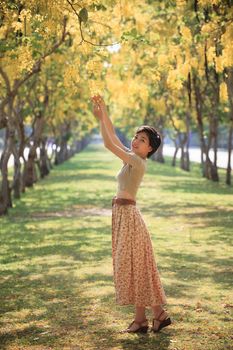 portrait of young beautiful asian woman relaxing emotion in yellow blooming flowers park with happy face against bright and vibrant garden background
