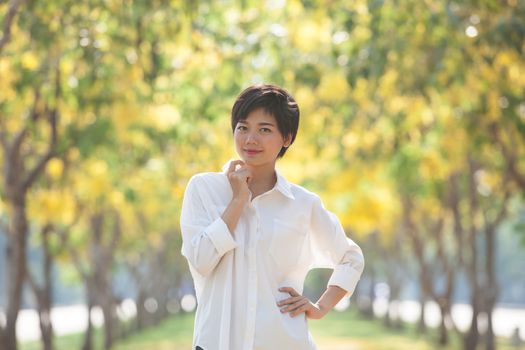 portrait of young beautiful asian woman with white shirt standing and smiling face in blur yellow flowers blooming background use for people and summer activities on location